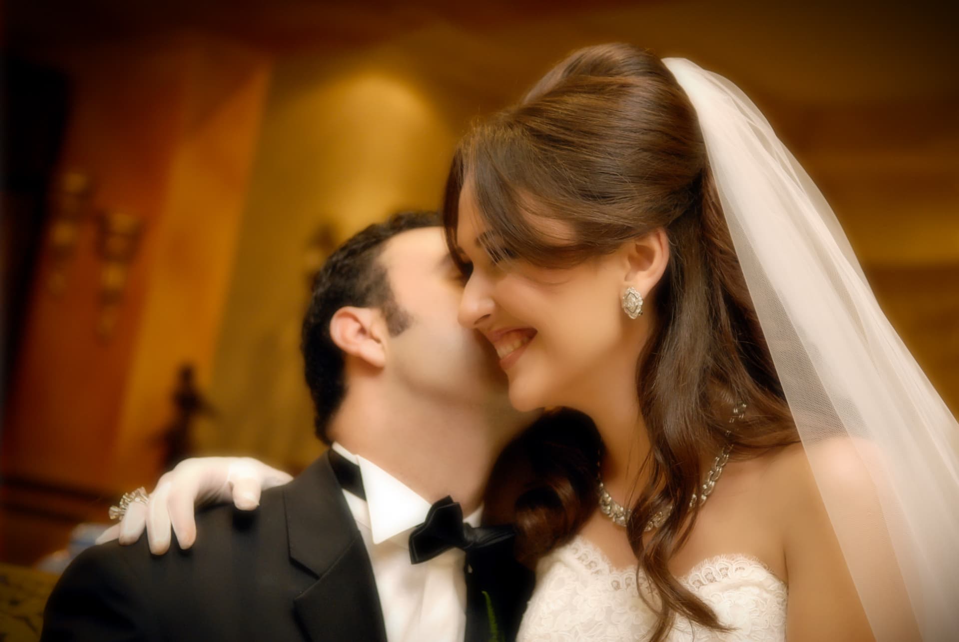 Groom kissing the smiling bride's cheek in warm light