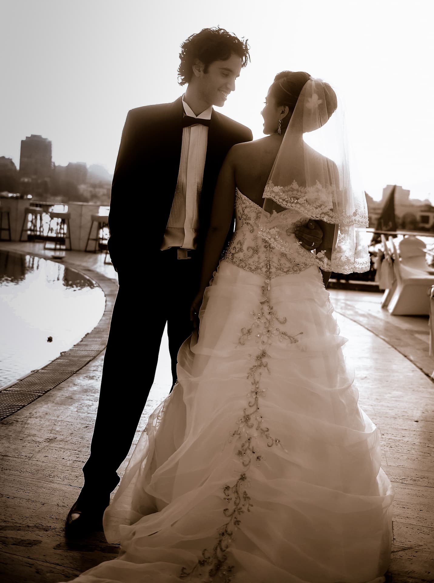 Bride and groom facing each other in soft backlight by the water
