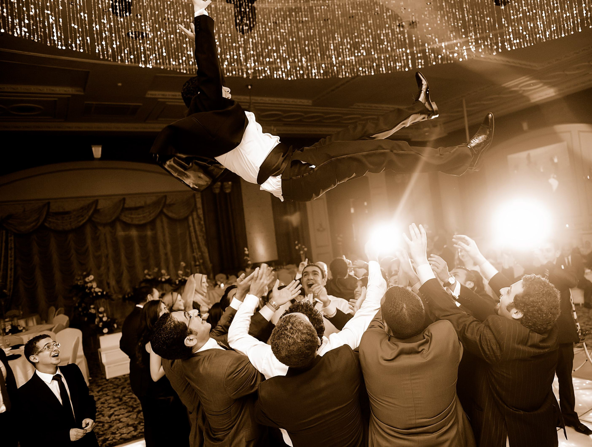 Groomsmen tossing the groom into the air beneath sparkling lights