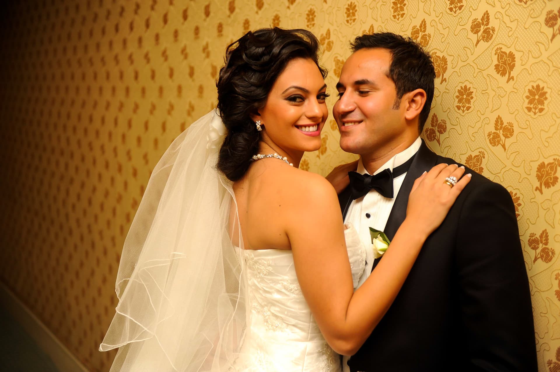 Bride and groom laughing against patterned wallpaper