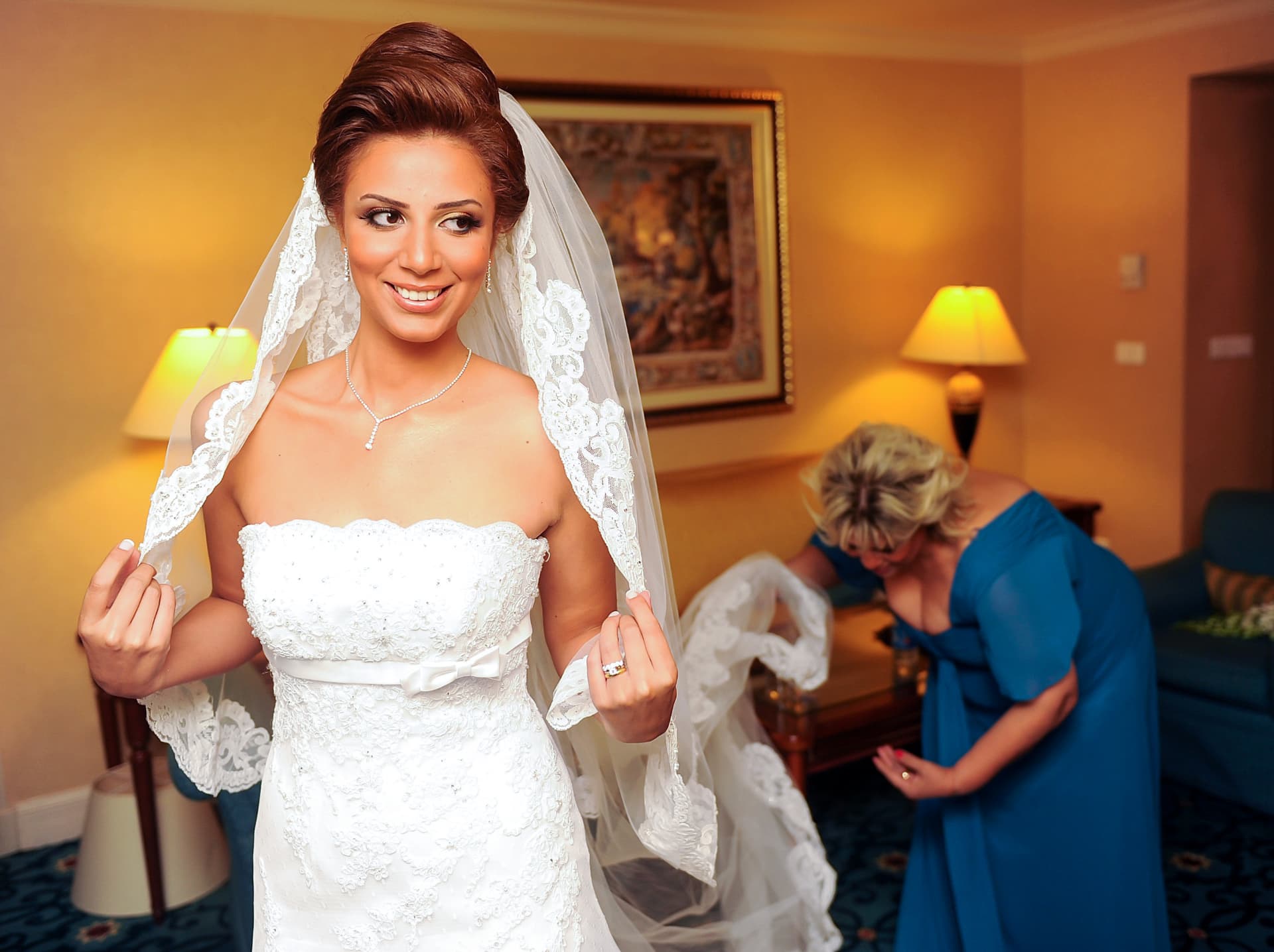 Bride adjusting her lace veil while her mother helps behind