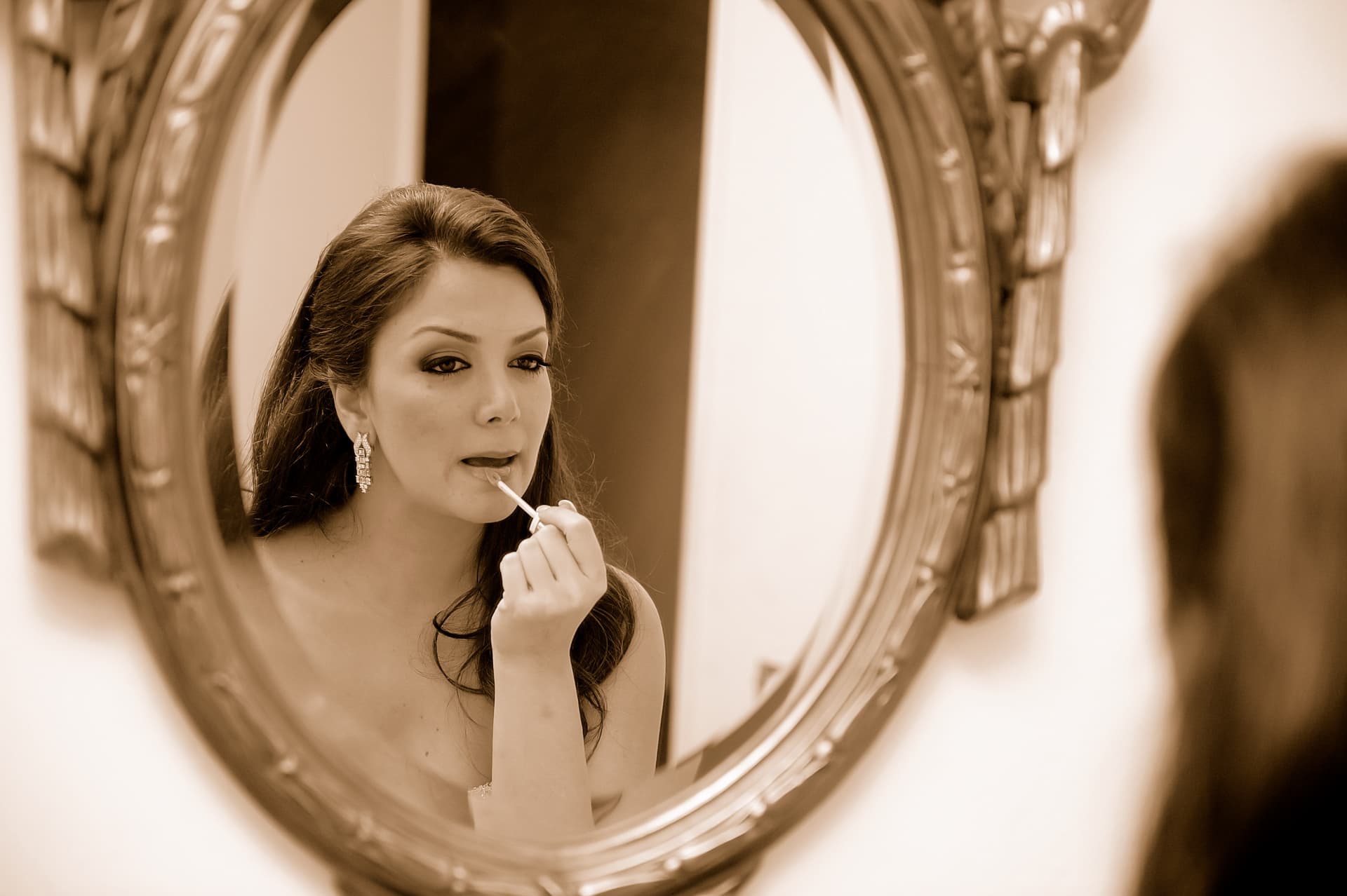 Bride finishing her makeup in an oval mirror in sepia