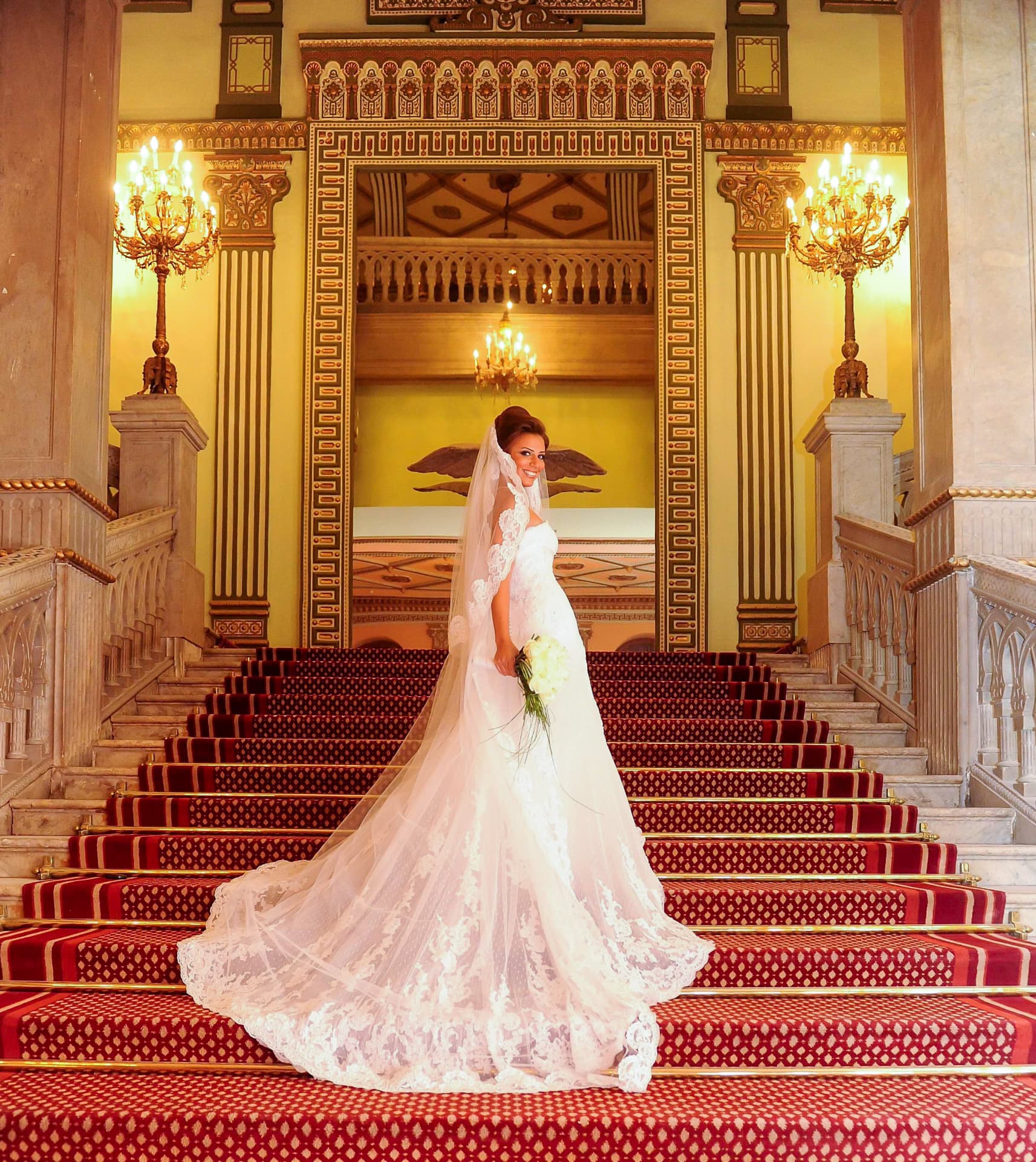 Bride on a grand red-carpeted staircase with her lace veil spread out