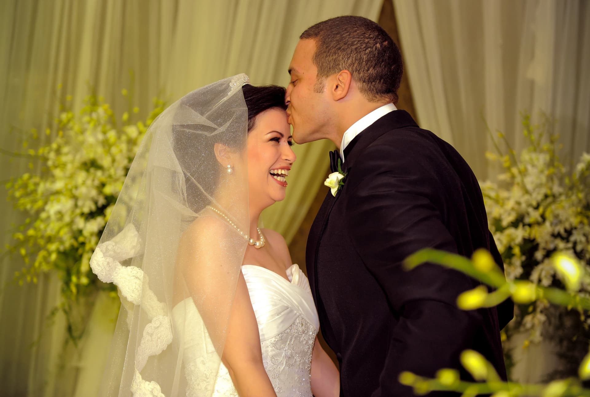Groom kissing the laughing bride's forehead at the ceremony