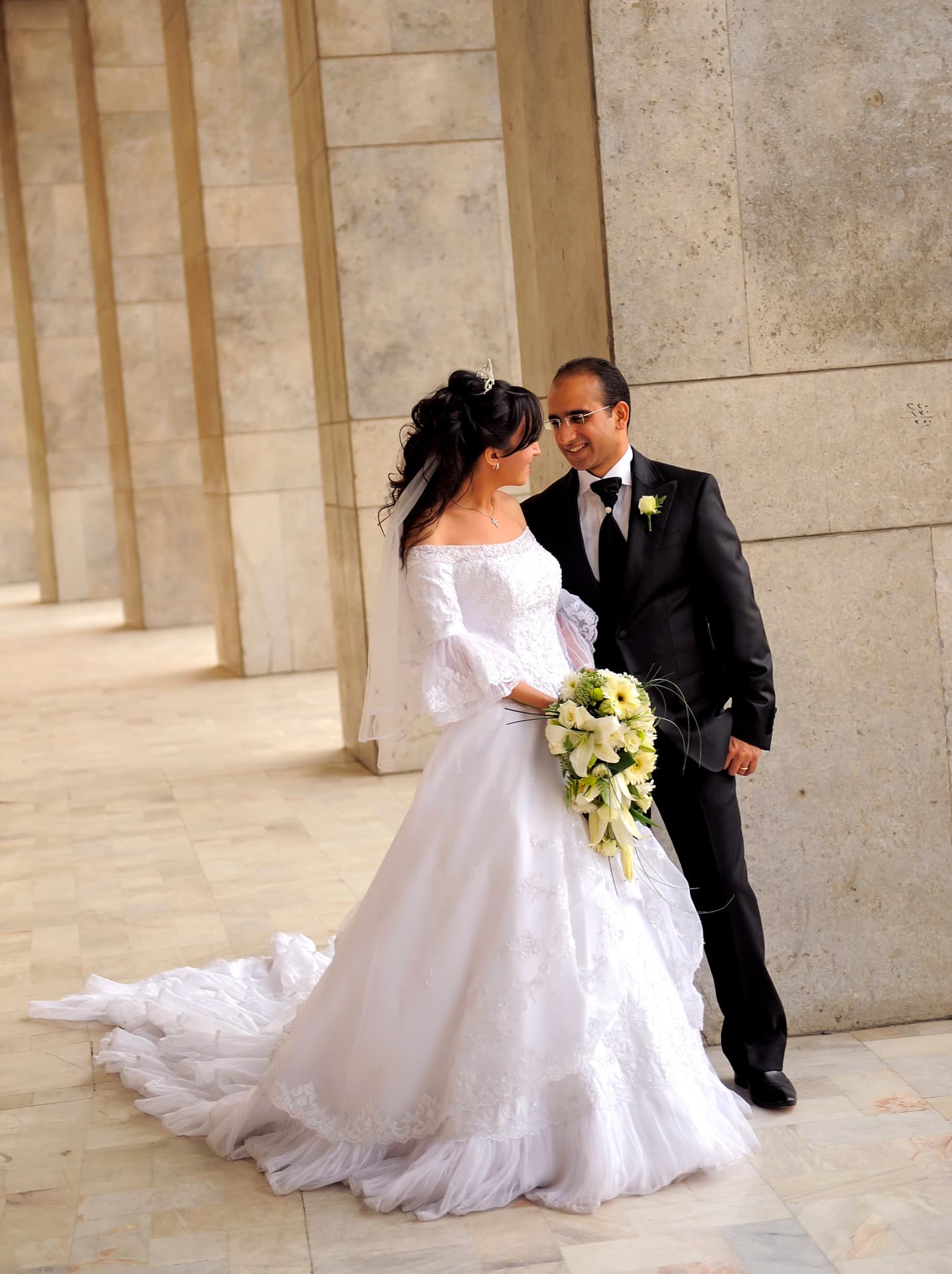 Bride and groom walking together through a marble colonnade