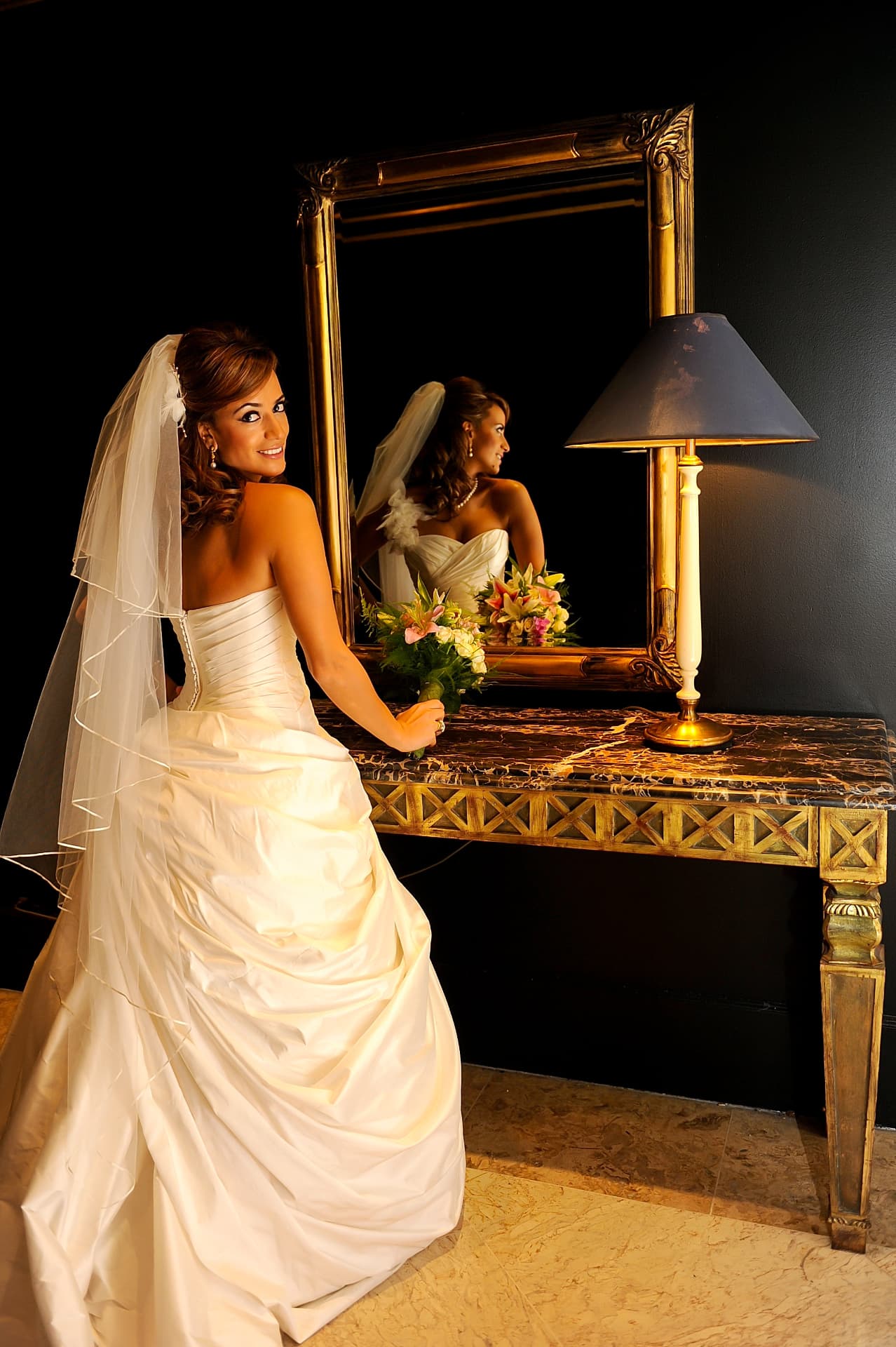 Bride looking back beside a gilded mirror in warm lamplight