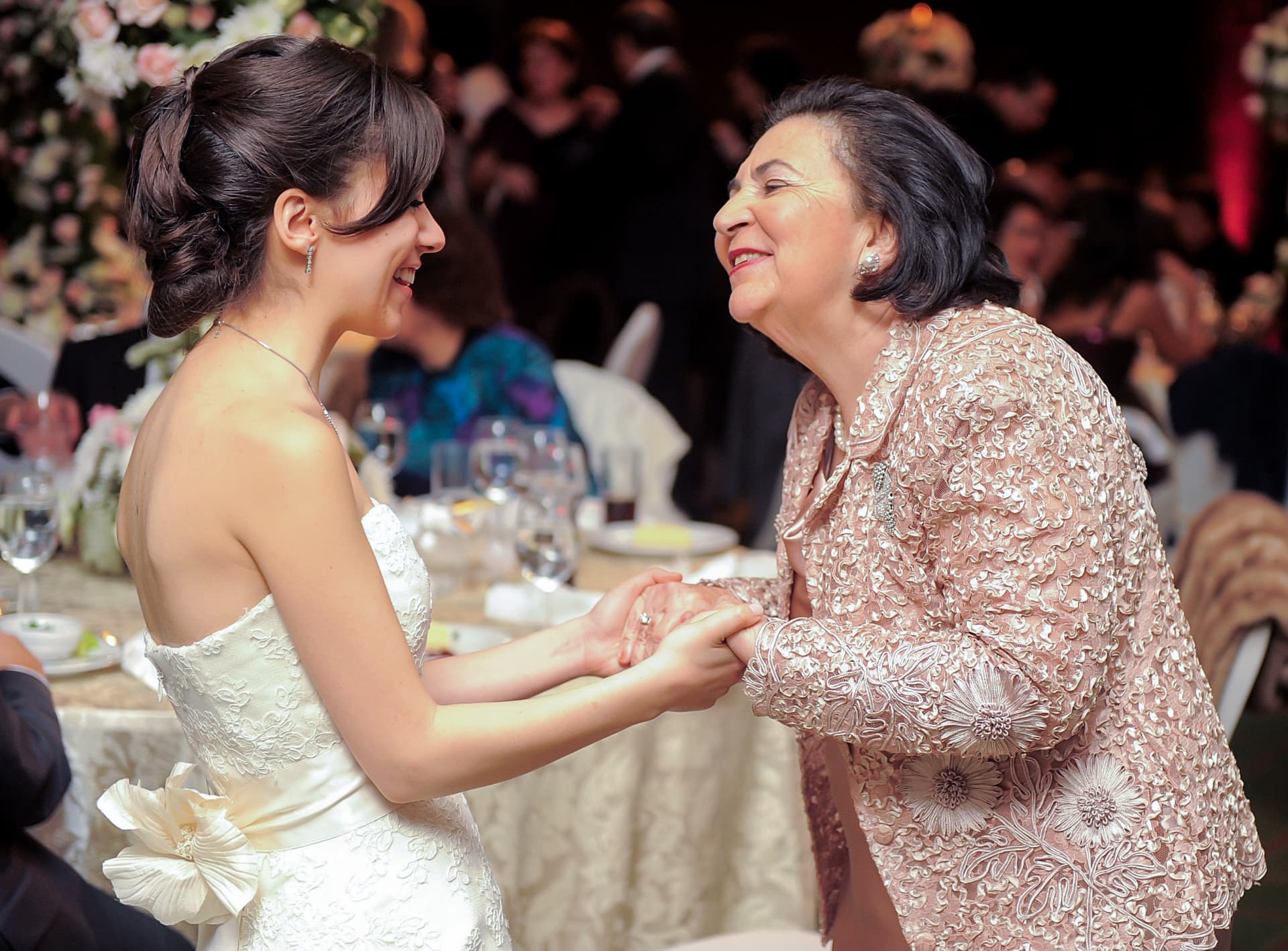 Bride laughing and holding hands with her mother at the reception