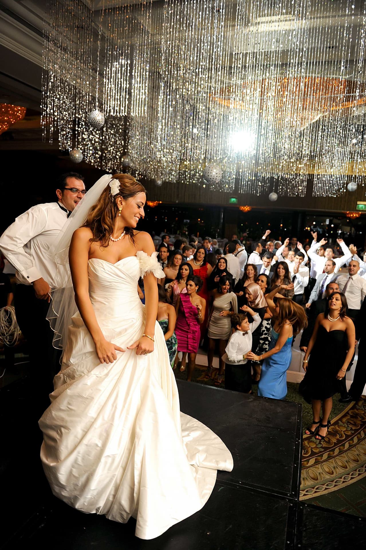 Bride dancing on stage beneath sparkling strands as guests cheer
